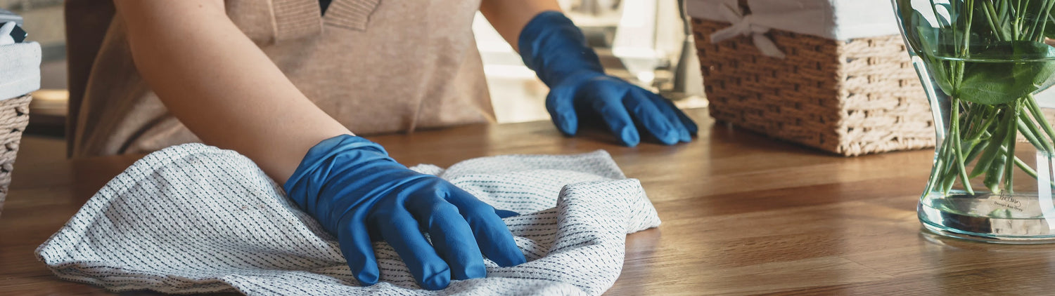A close up of an individual wearing blue cleaning gloves cleaning a wooden countertop