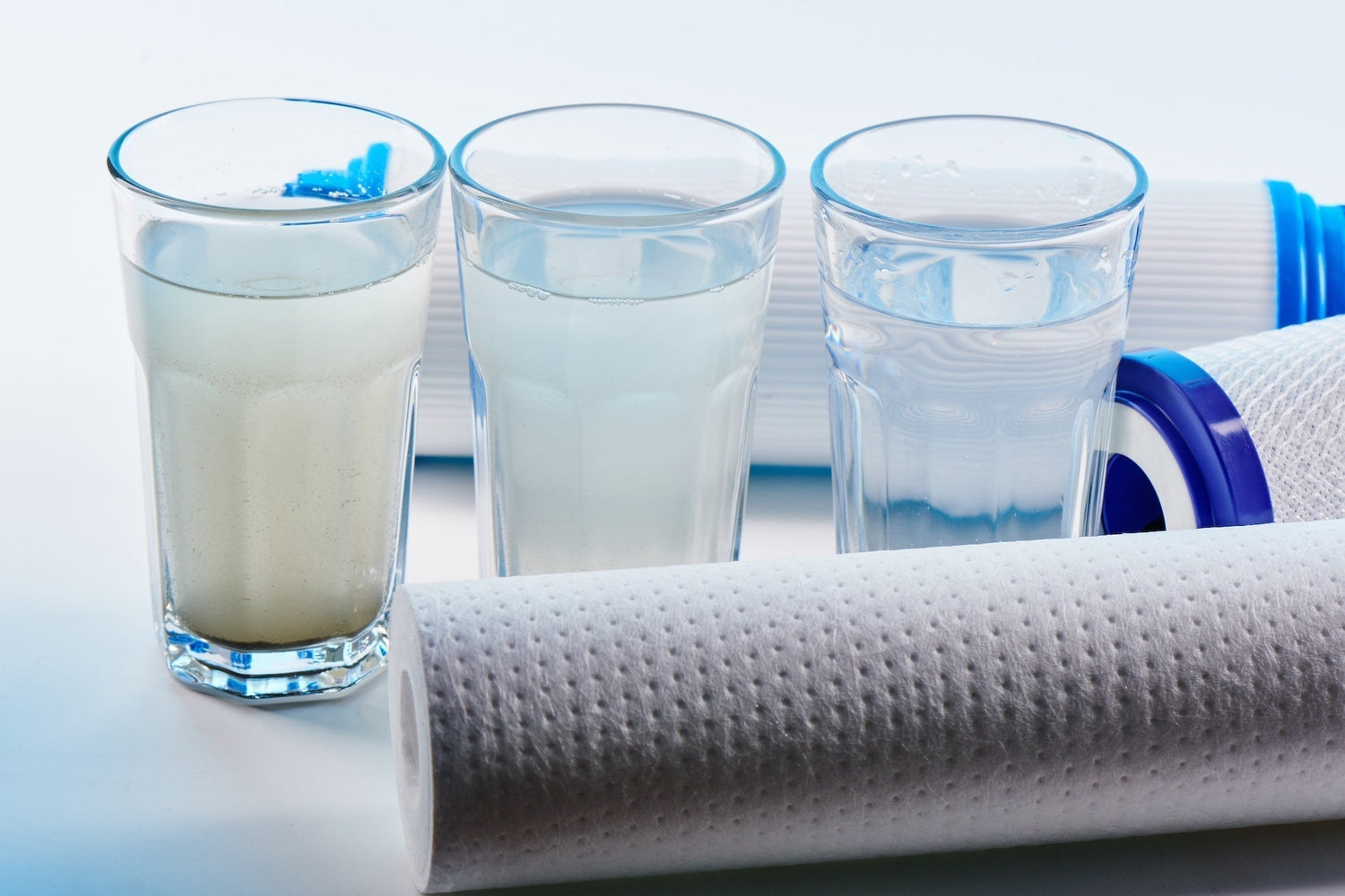 3 glasses of water, two cloudy, and one clear, surrounded by water filters