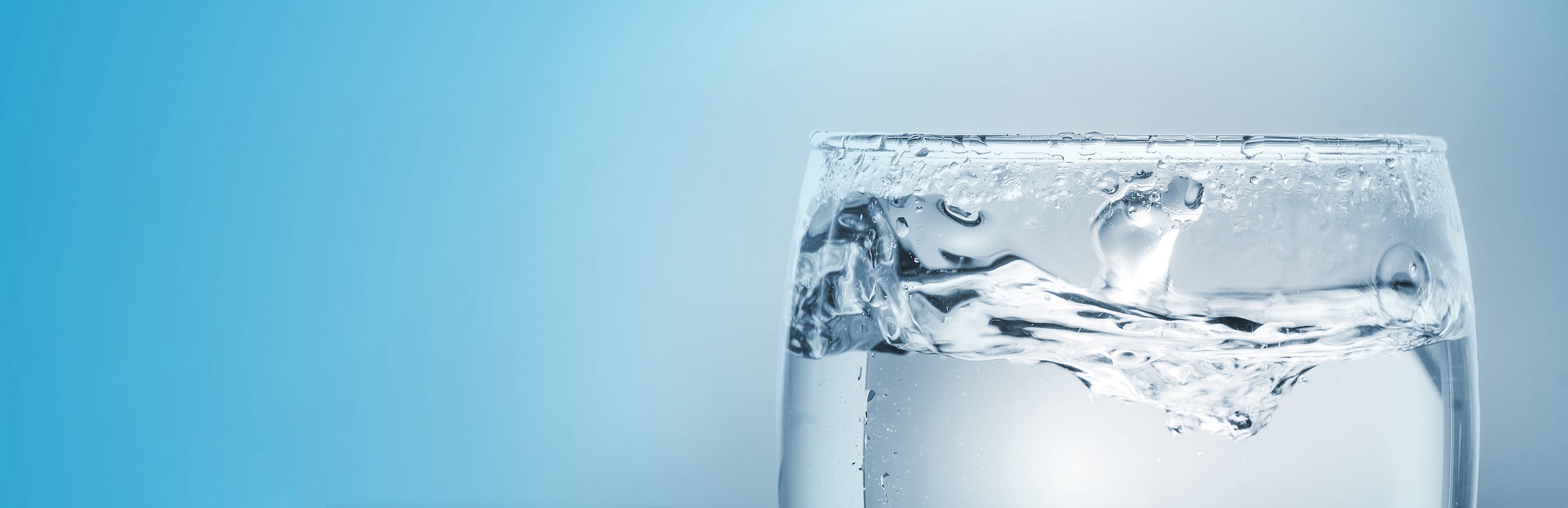 a blue background with the top of a full glass of water in the right corner of the image
