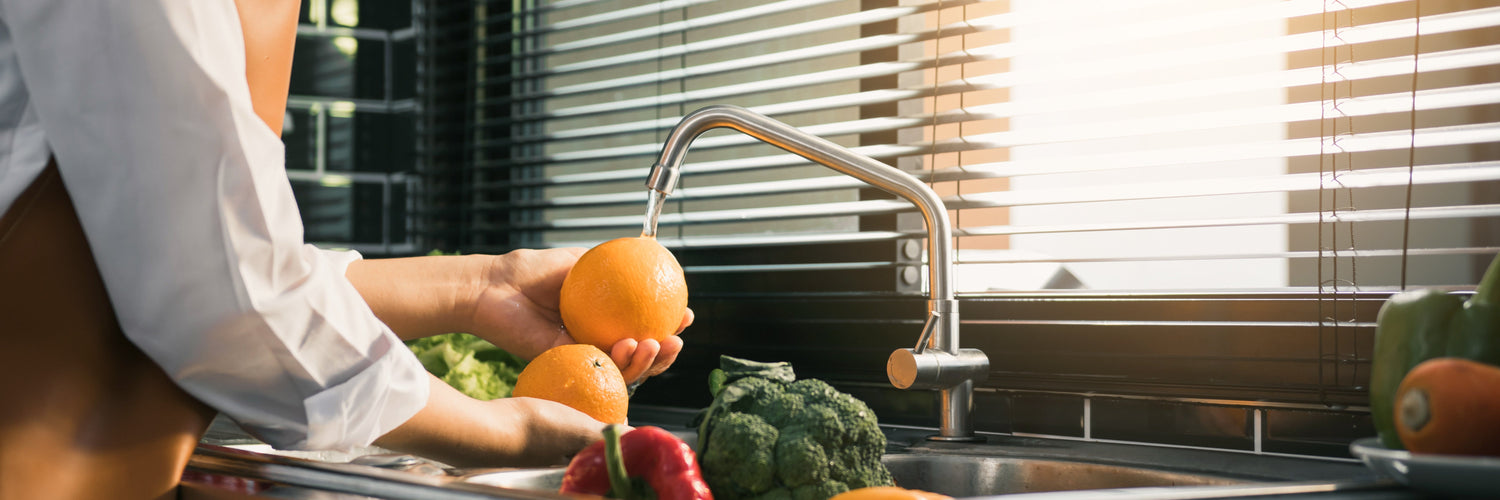 a woman washing produce in a kitchen sink area