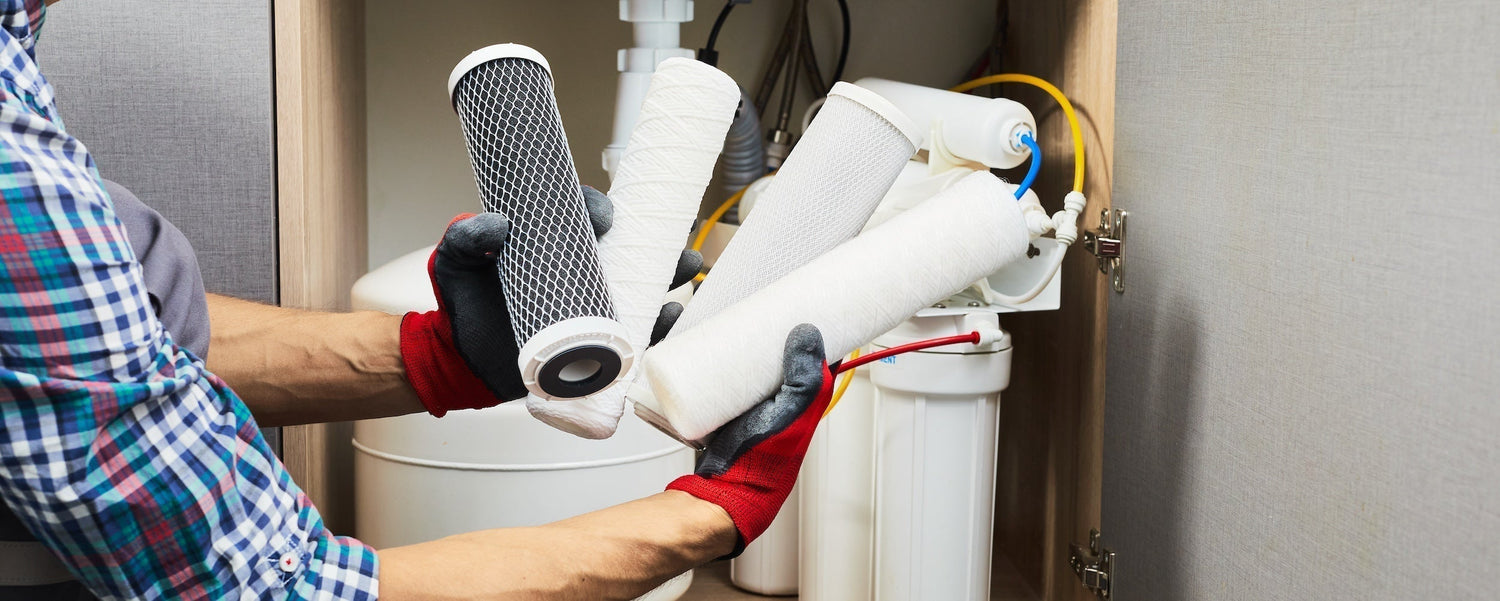 A plumber holding up various water filter replacements