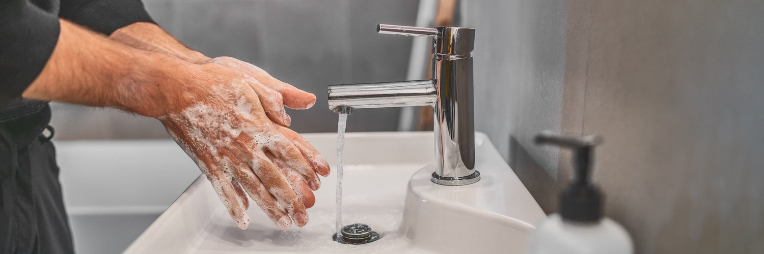 a man in a robe washing his hands at the bathroom sink, soap suds on his hands