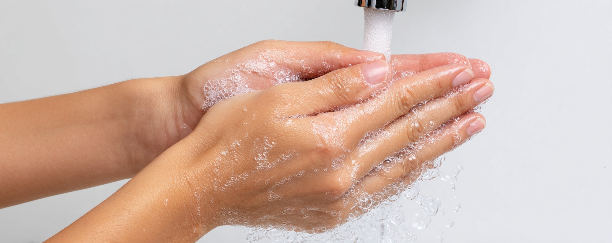 two hands, slightly soapy, clasped together under a running faucet